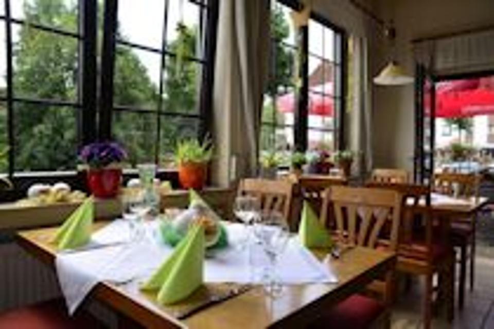 Hübsch gedeckter Tisch im hellen Gastraum mit großen Fenstern, weiße Tischdecke, grüne aufgestellte Servietten