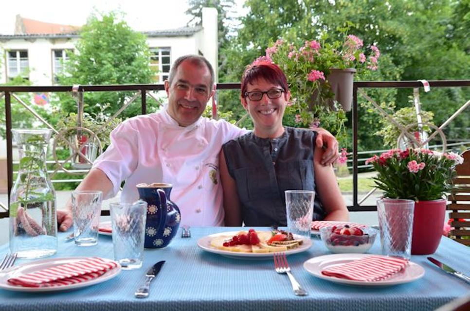 Die Gastgeber Andrea und Dieter Mohr sitzen freundlich lächelnd an einem hübsch gedeckten Tisch.