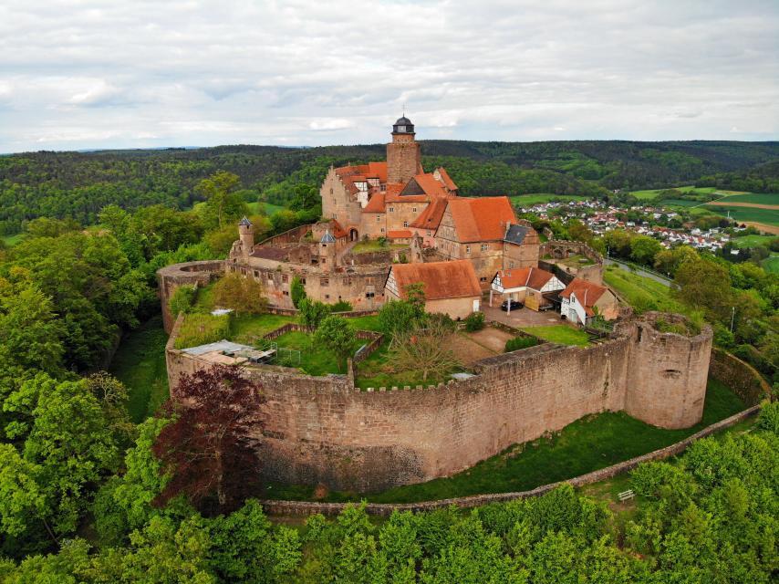 Blick auf die Burg Breuberg aus der Vogelperspektive umgeben von Wäldern oberhalb des Mümlingtals
                 title=