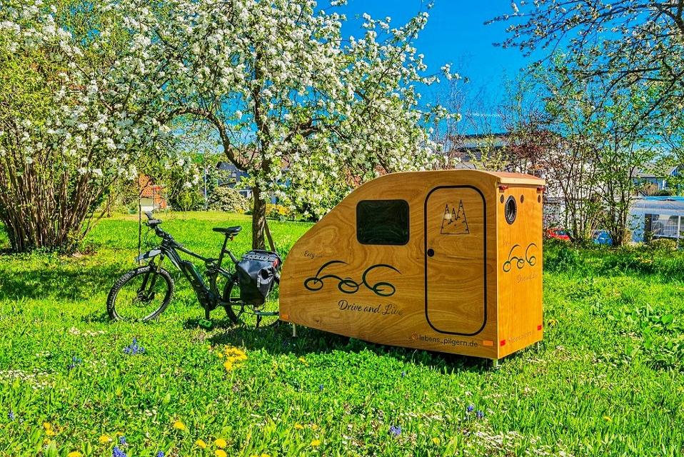 Aktiv in der Natur unterwegs sein und die schönsten Übernachtungsplätze suchen mit einem formschönen Fahrrad-Wohnwagen für E-Bikes aus natürlichem Holz. 