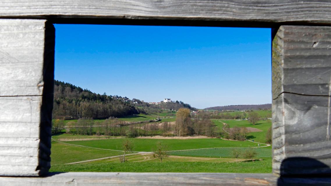Blick durch einen Holzrahmen in die Landschaft mit dem weißen Renaissanceschloss Lichtenberg im Hintergrund
