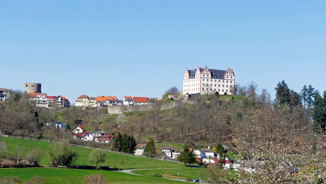 Blick auf das weiße Renaissanceschloss Lichtenberg und das Bollwerk vor frühlingshafter Landschaft