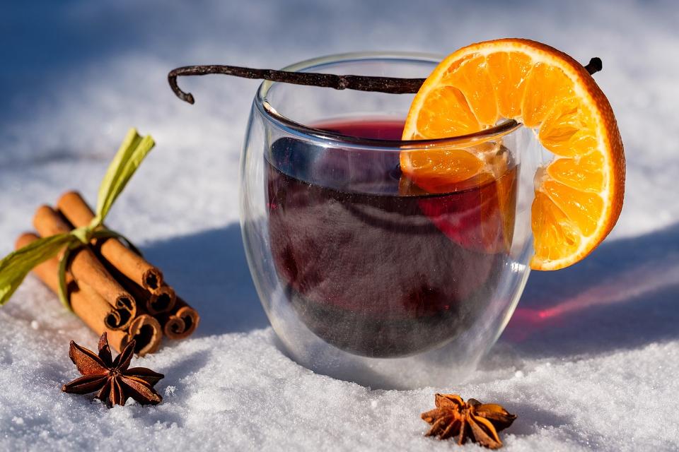 Glühweinglas im Schnee mit Deko aus Orangenscheibe, Zimtstangen und Nelken