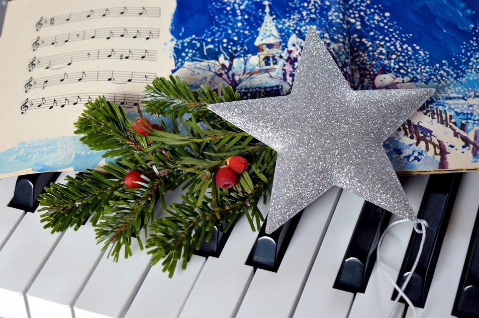 Silberner Weihnachtsstern mit Eibenzweigen auf Notenblatt mit Winterlandschaft auf einer Klaviertastatur