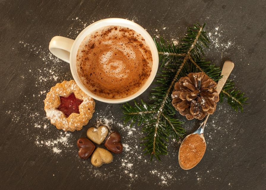 Plätzchen  und Tasse Kakao, dekoriert mit Tannenzweig, Zapfen, Löffel mit Kakaopulver und mit Puderzucker bestreut
