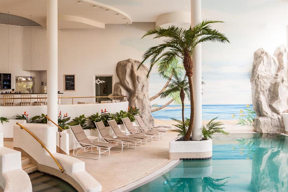 Das Hallenbad beinhaltet Liegestühle und dekorative Palmen und Gesteine