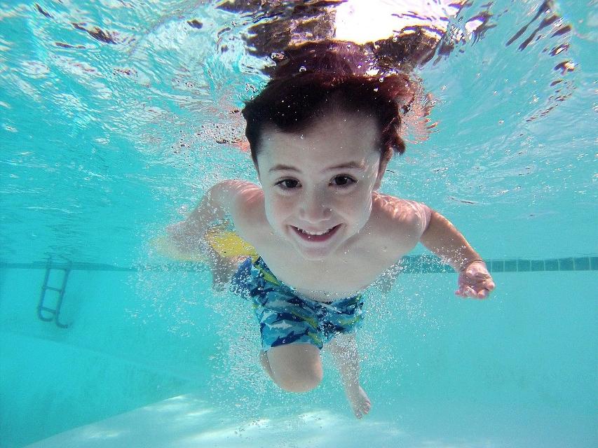 Kind taucht im Wasser und schaut dabei in die Kamera.