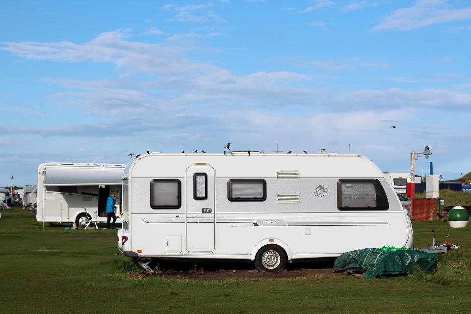 Wohnwagen steht auf dem Campingplatz. Im Hintergrund ist blauer himmel zu sehen.