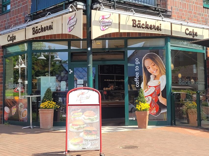 Eine Bäckerei mit über Eck verglaster Front. Darüber steht, in braunen Buchstaben auf beigem Hintergrund Bäckerei und Cafè Tamke.