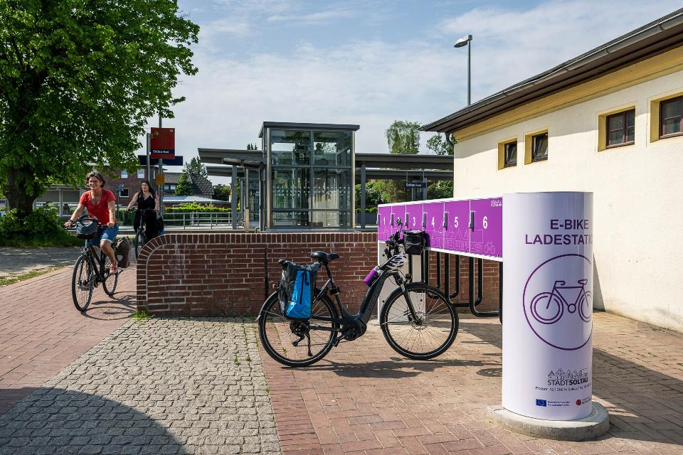 Am Bahnhof Soltau im Zugangsbereich zum Gleis 1 steht eine Ladestation für 6 E-Bikes. Die Station ist in freundlichem lila gestaltet.