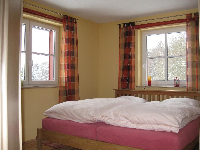 Blick in das Schlafzimmer mit großem Doppelbett und zwei Fenstern