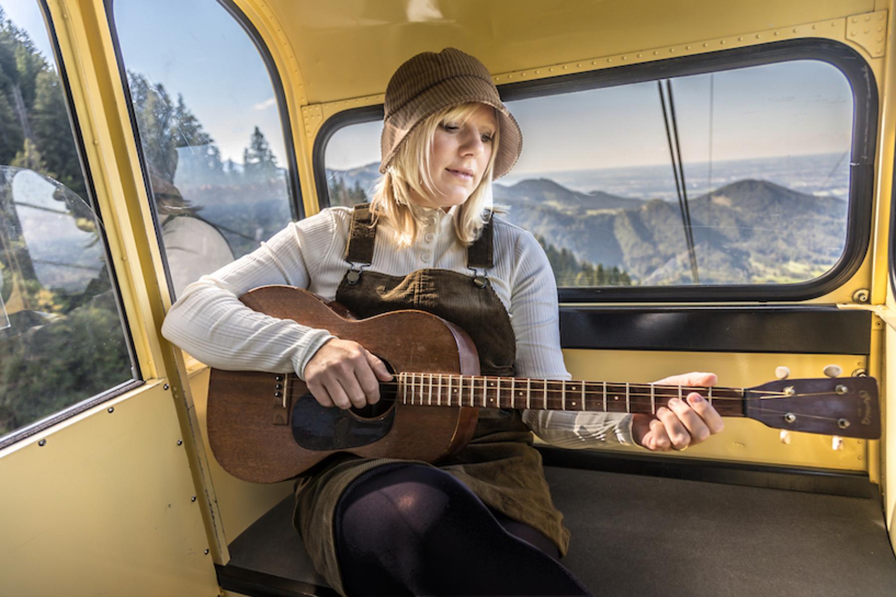 Claudia Koreck mit Gitarre und Hut in einer Gondel in den Bergen