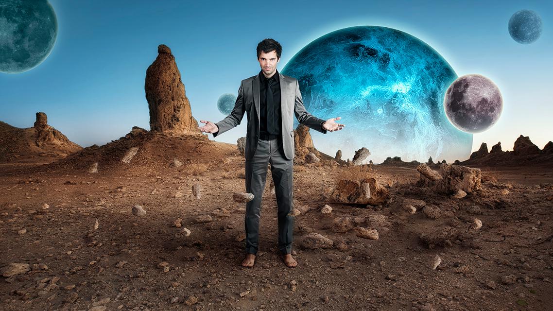 Ein Mann steht in der Wüste. Hinter ihm sieht man eine Art riesigen Mond.