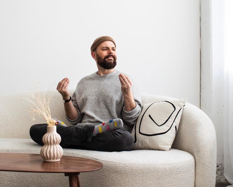 Patrick Salmen sitzt im Schneidersitz auf einem Sofa und meditiert. 