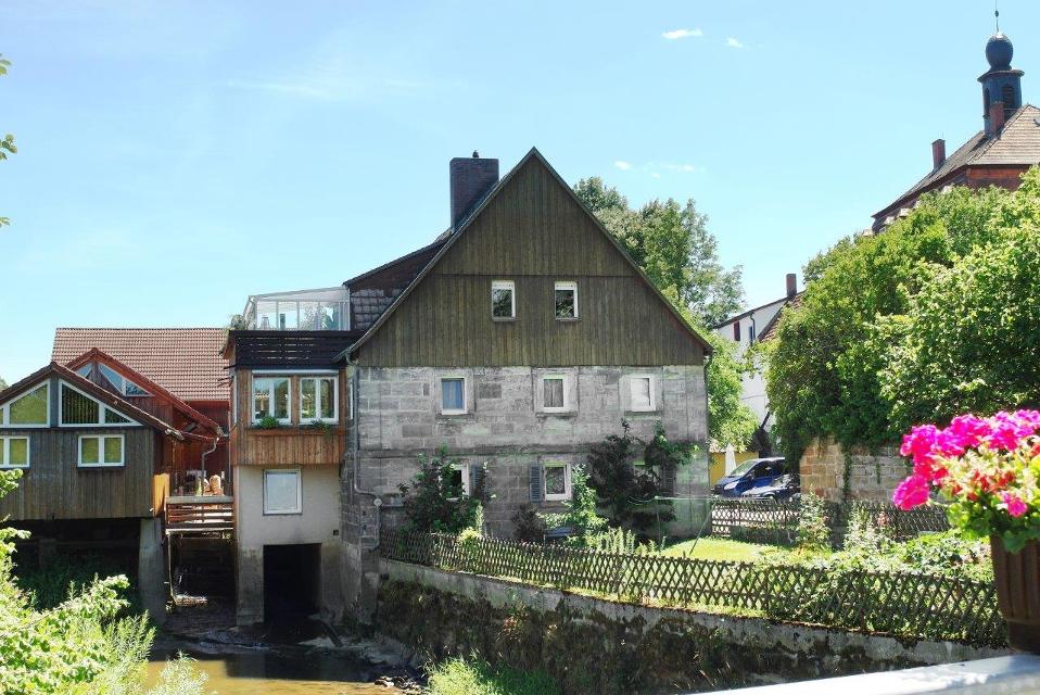 Frontansicht auf das Gebäude der Mühle Altenplos mit dem Roten Main davor. 