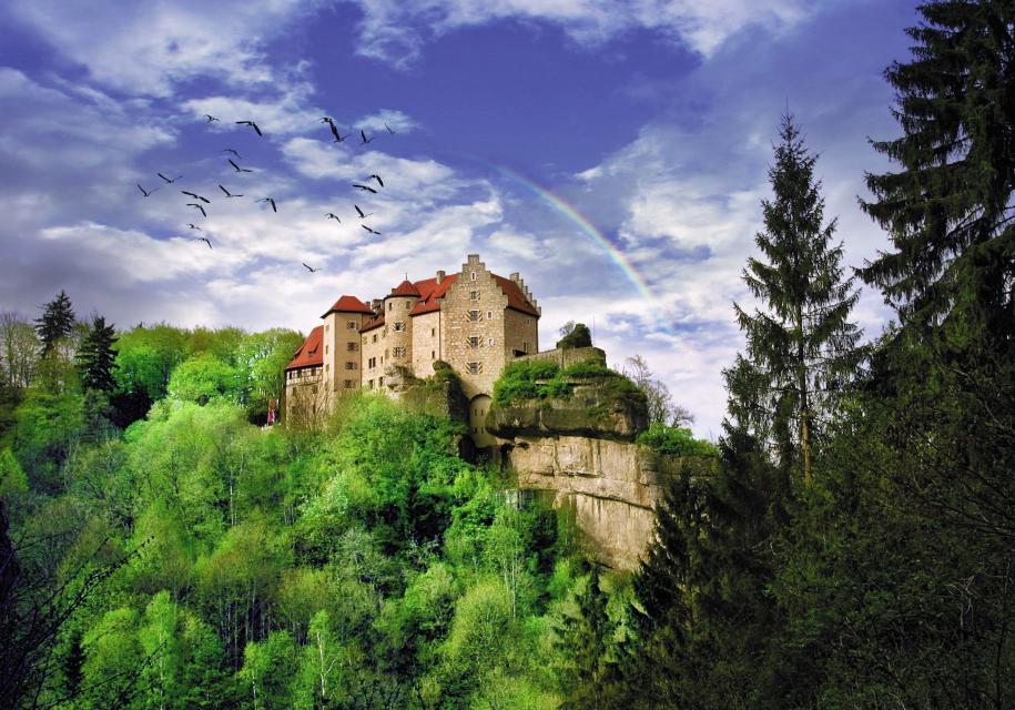 Ein Vogelschwarm am teils bewölkten Himmel und ein hinter der Burg im halbkreis stehender Regenbogen umhüllen die Burg und verleihen einen mystischen Gesamteindruck.