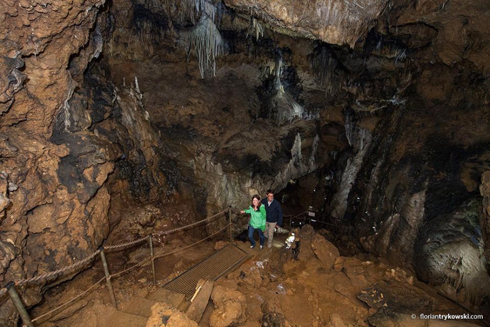 Ein Mann und eine Frau laufen auf einem Weg mit Geländer in der Höhle bergauf und bewundern die umliegenden Tropfsteine.