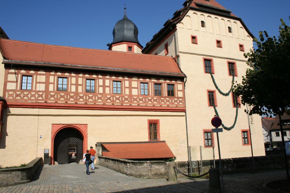 Ein mächtiges, altes Gebäude mit einem hölzernen Tor. Die Fassade vom zweiten Stockwerk ziert ein rotes Fachwerk.