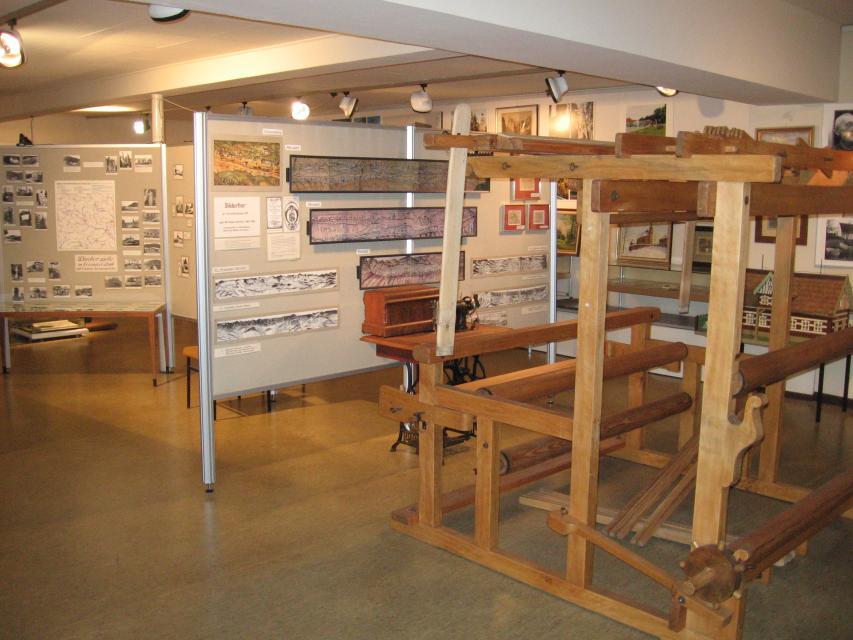 Innenansicht des Museums. Im Vordergrund ein alter Webstuhl aus Holz. Im Hintergrund Vitrinen mit Ausstellungsstücken.