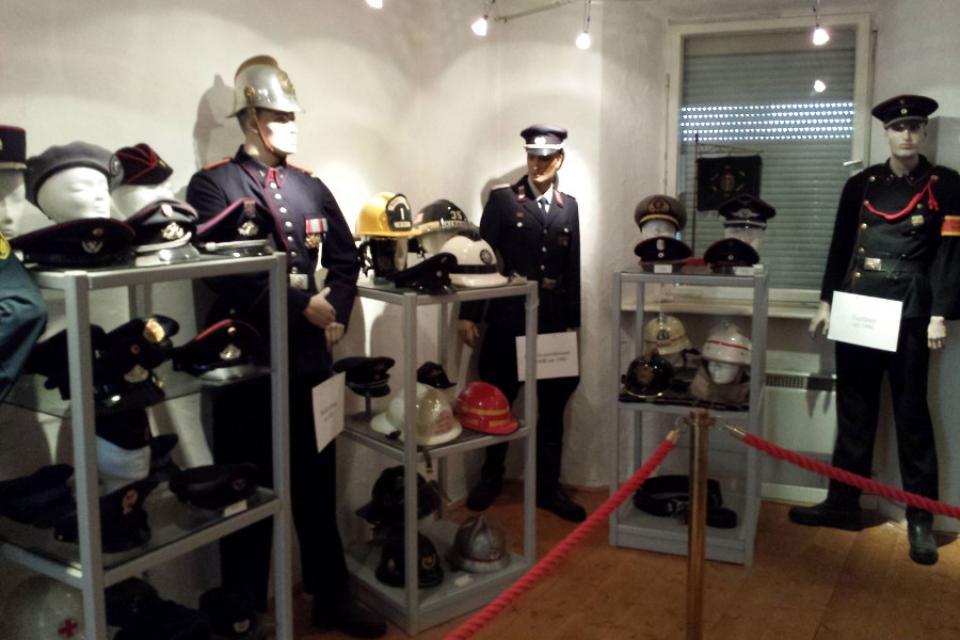 Ausstellungsraum mit drei lebensgroßen Puppen in alter Feuerwehrmontur sowie weiteren Ausstellungsstücken in offenen Regalen.