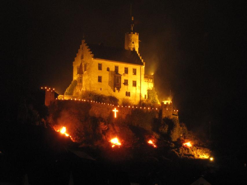 Eine große Anzahl an Wachslichter und ein beleuchtetes Kreuz ummalen die Felsen und Burgmauern der Gössweinsteiner Burg. Ebenfalls sieht man ein beleuchtetes Kreuz.