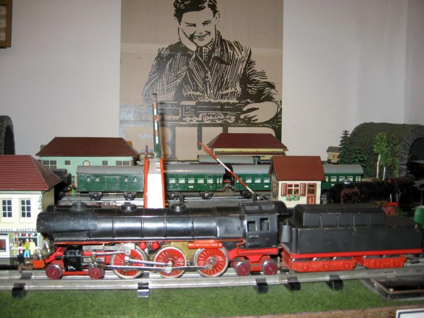 Vor Modellhäusern steht eine schwarz-rote Modelleisenbahn (Lok) mit Kohlewagen.