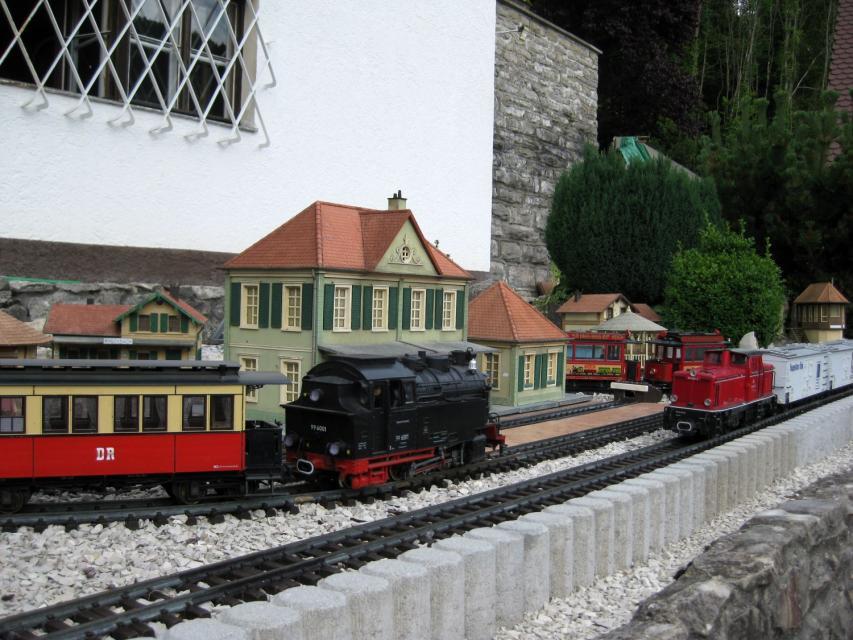 Eine Modelleisenbahn mit zwei Loks und einem grünen Bahnhofsgebäude.