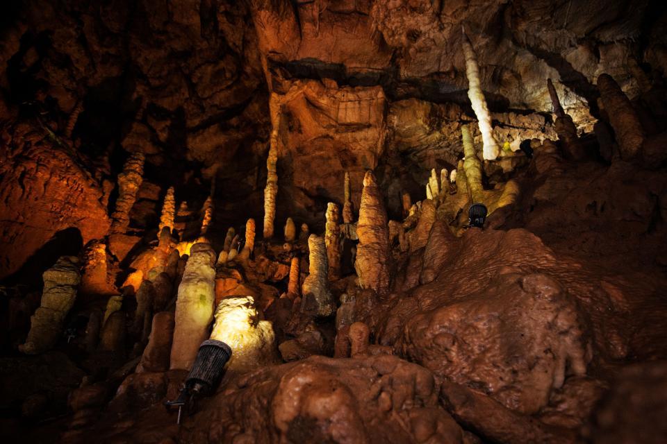 Ein Strahler beleuchtet in der Höhle viele kleine aufragende Tropfsteine.