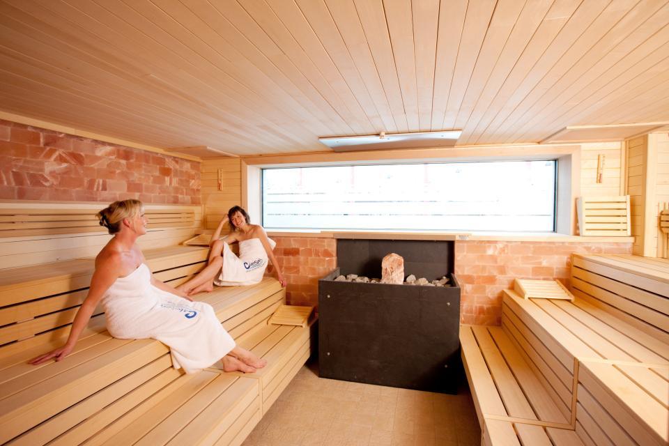 Zwei Frauen sitzen auf Holzbänken in der Sauna.