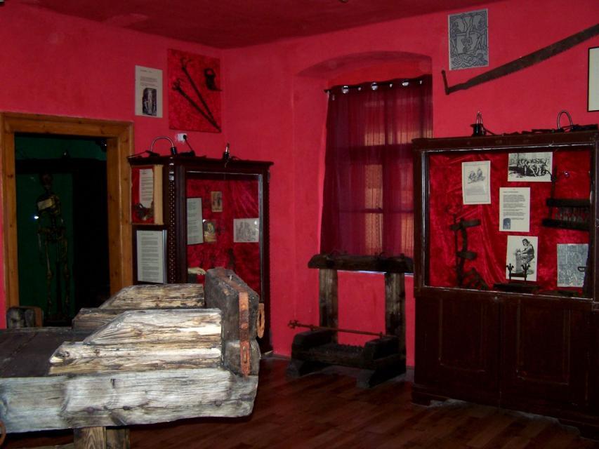 In einem Ausstellungsraum mit roten Wänden stehen verschiedenen Vitrinen. Die Ausstellungsstücke sind zu klein abgebildet, um sie zu erkenne.