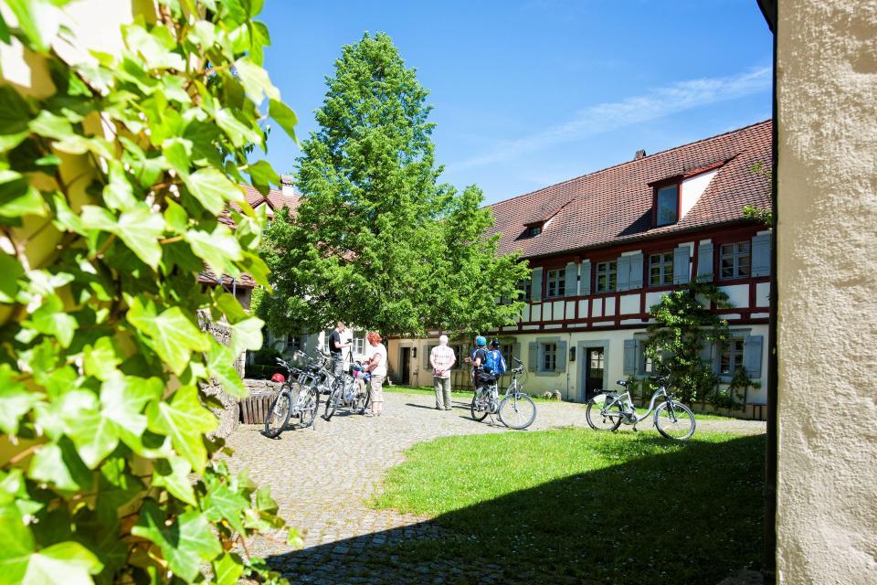 Im gepflasterter Innenhof des Museums stehen Besucher mit ihren Fahrrädern. Umrahmt wird der Hof von rot weißen Fachwerkhäusern.
                 title=