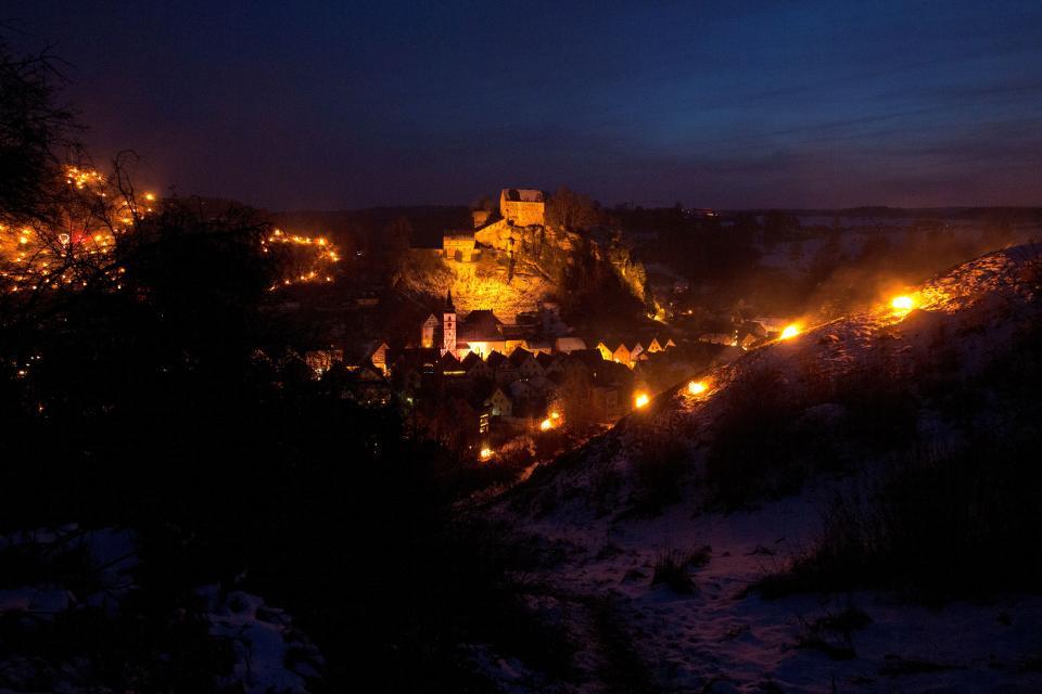 Nächtliche Ansicht der Ewigen Anbetung in Pottenstein. Unzählige Holzfeuer schmücken die Berghänge. Auch die Burg ist in warmen Licht erleuchtet.
