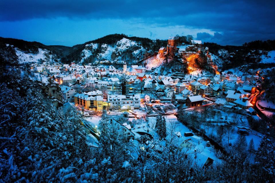 Pottenstein wurde sichtlich reich mit Schnee beschenkt. Die Häuser sind mit Schnee bedeckt. Beleuchtete Felsen und abendlich beleuchtete Straßenlaternen bilden eine romantische Stimmung im Ort.