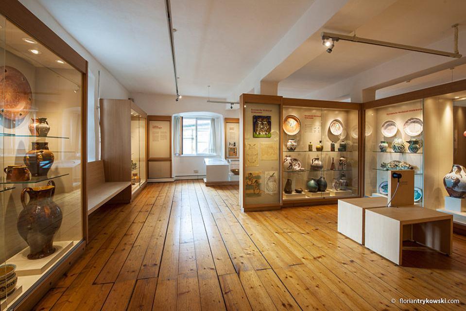 In einem großen Raum mit Holzdielenboden stehen an den Wänden beleuchtete Vitrinen, in denen verschiedenen Töpferwaren ausgestellt sind.
