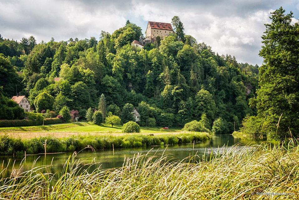 Hoch über dem Wiesenttal, durch welches sich der namentlich identische Fluss züngelt, sieht man die hochmittelalterliche Adelsburg. Zwischen den grünen Wäldern spitzen zwei Fachwerkhäuser hervor.