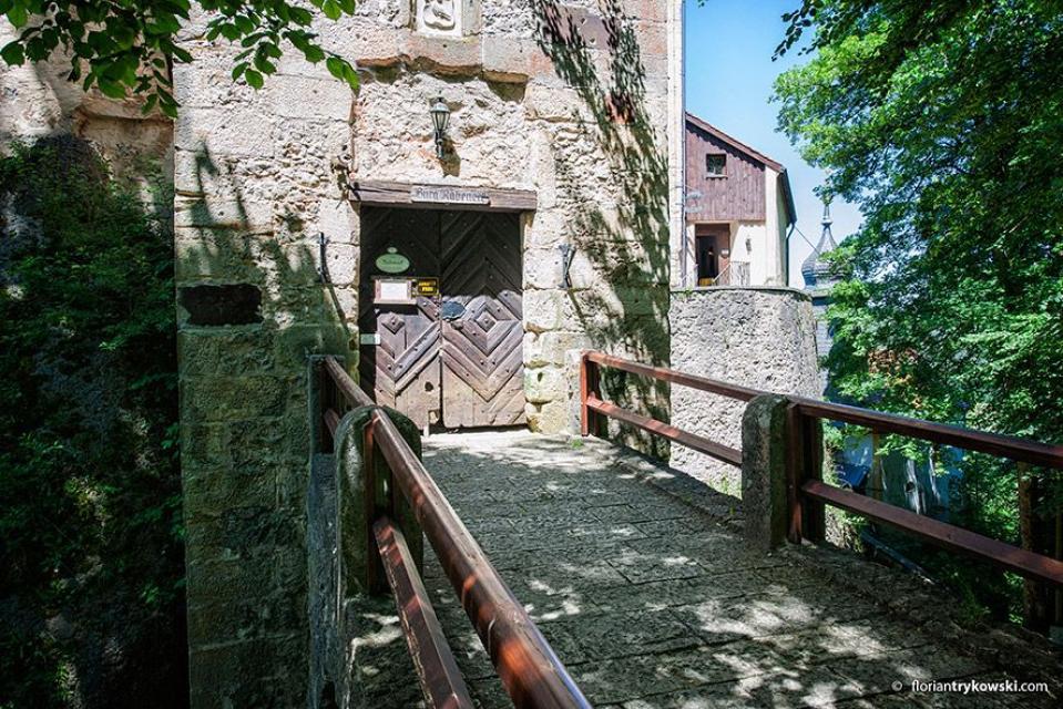Über eine Brücke gelangt man zum imposanten Eingangstor der Burg. Die Sonne erhellt die Front und den über der Tür angebrachten Schriftzug "Burg Rabeneck".