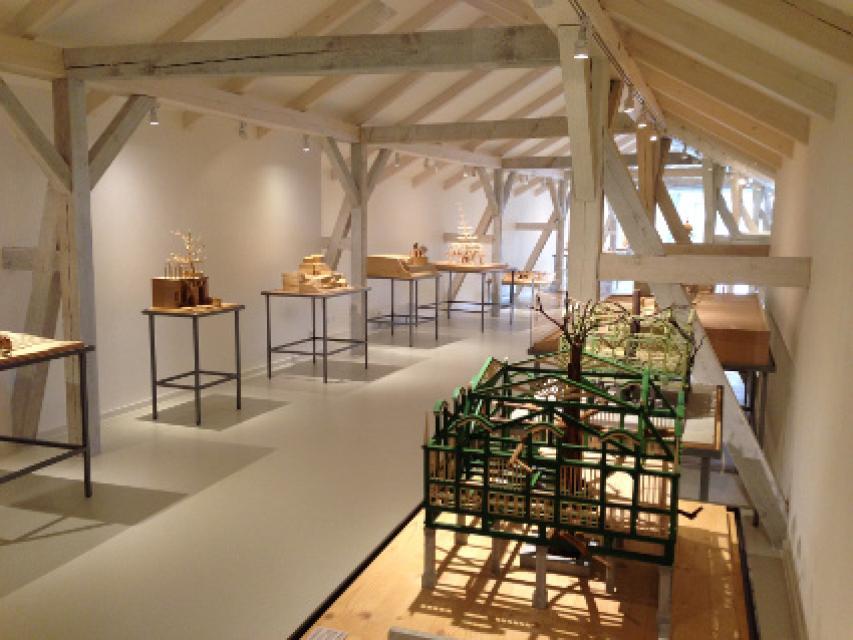 Ein heller Raum mit weißen Balken, in dem auf filigranen Tischen Lindenbaum-Modelle stehen.