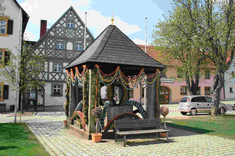 Am Marktplatz steht ein Brunnenhaus mit schwarzen Schieferdach. Vom Dach hängen rings um Girlanden aus bunten Ostereiern.