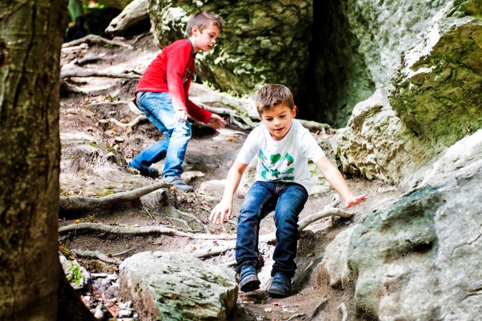 Zwei Buben üben Geschicklichkeit, indem sie kleine Felsen im Wald hinunter klettern