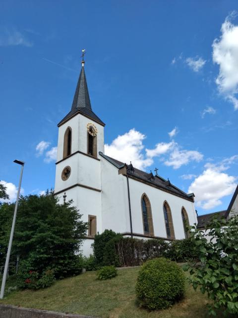 Umgeben von grünen Büschen und Sträuchern steht die Kirche Kremmelsdorfs im Ort.