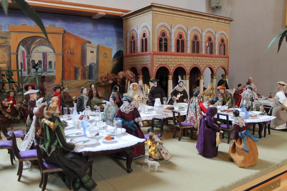 Kleine Figuren, welche an gedeckten Tischen sitzen. Die Situation zeigt ein Brautpaar mit seinen Gästen "Die Hochzeit zu Kana"