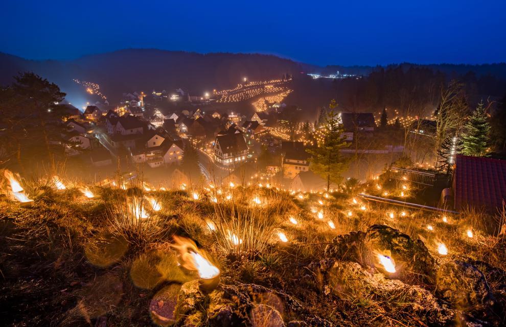 Umrandet von hunderten, brennenden Wachslichtern führt der Blick auf den Ort im Tal bei Nacht.