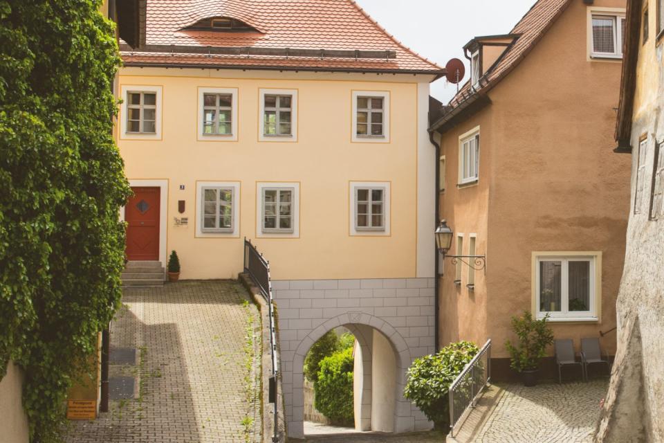 Durch ein altes Haus mit roten Dachziegeln und gelber Fassade führt durch ein Tor eine Straße.