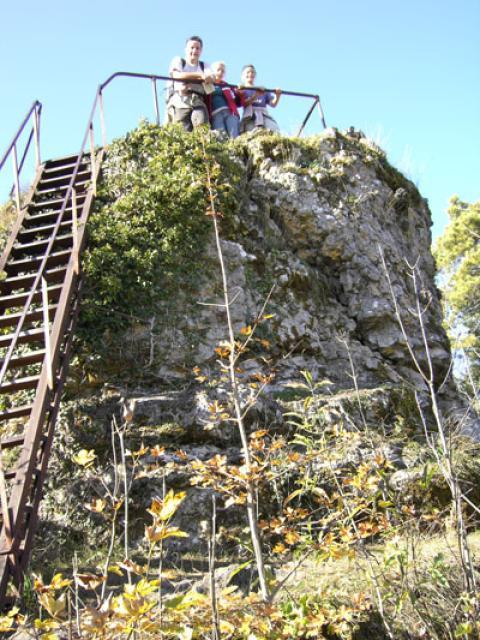 Auf einen mächtigen Naturfels führt eine Stahltreppe mit Geländer. Auf dem Fels sind drei Personen zu erkennen.
                 title=