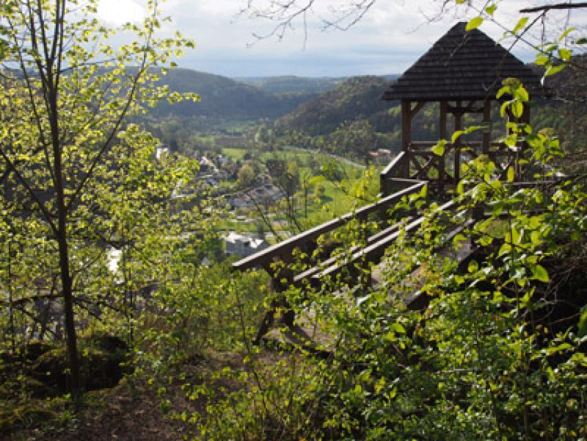 Zwischen Büschen und kleinen Bäumen führt eine hölzerne Brücke hinüber zum Aussichtspavillon mit Blick in das Wiesenttal.