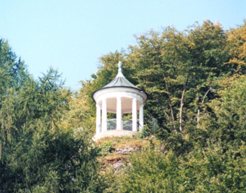 Nahaufnahme des weißen, runden Pavillons mit Spitzdach inmitten von Bäumen.