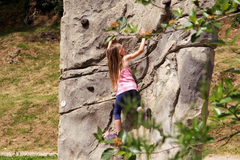 Ein junges Mädchen, dass eine Art Boulderwand hinauf klettert