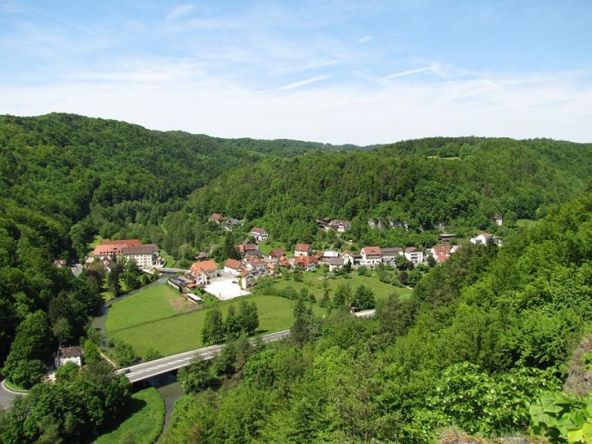 Blick auf den Ort in Tallage, umgeben von bewaldeten Bergen.
