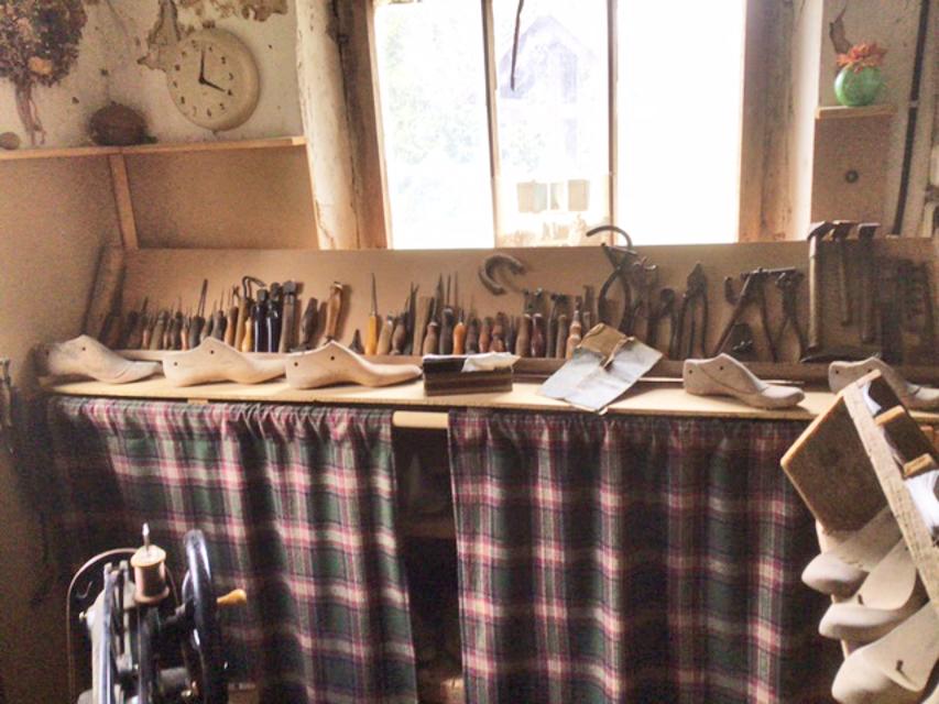 Auf einem Holzbrett liegen verschiedene Schusterwerkzeuge nebeneinander aufgereiht.