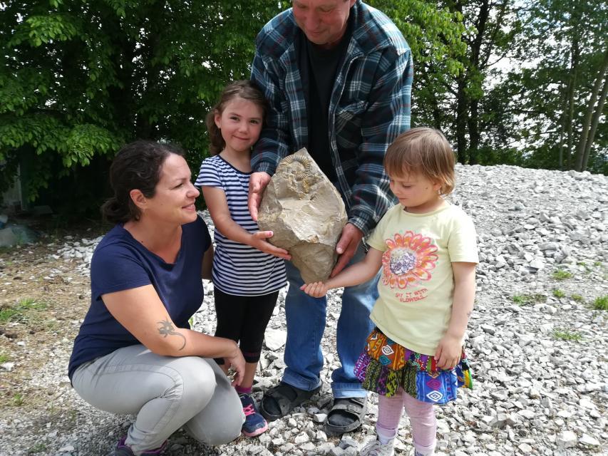 Vater, Mutter und zwei Kinder halten lächelnd einen großen Felsbrocken, in dem ein Fossil erkennbar ist.